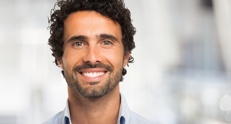 A man with curly dark hair smiling, to represent either a dental veneer treatment or teeth bonding treatment from Snodgrass-King cosmetic dentistry