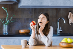 A girl sitting at a kitchen counter eating an apple, but she's looking at the apple because of her tooth sensitivity.