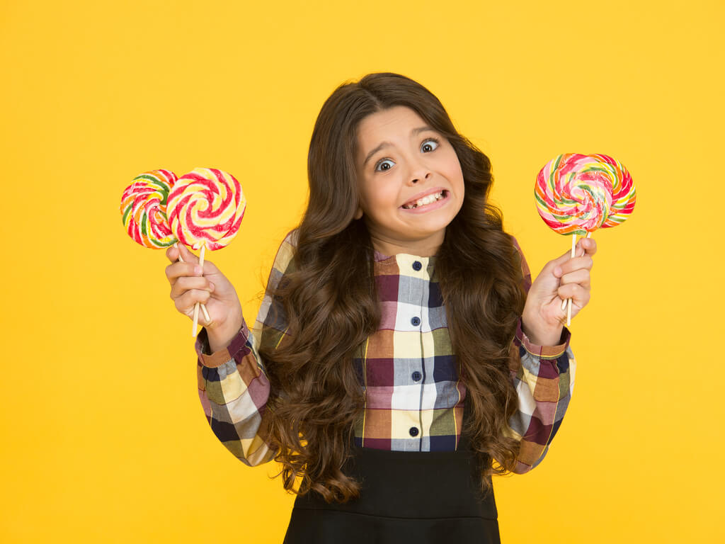 A little girl holding three lollipops. Keeping track of your oral health will help you avoid many health problems in the future.