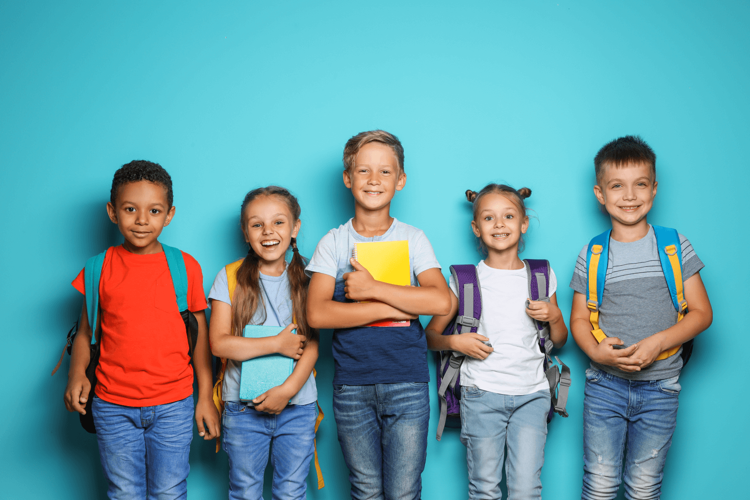 A group of kids standing in front of a blue wall, while smiling to show their healthy teeth, thanks to pediatric dentistry.
