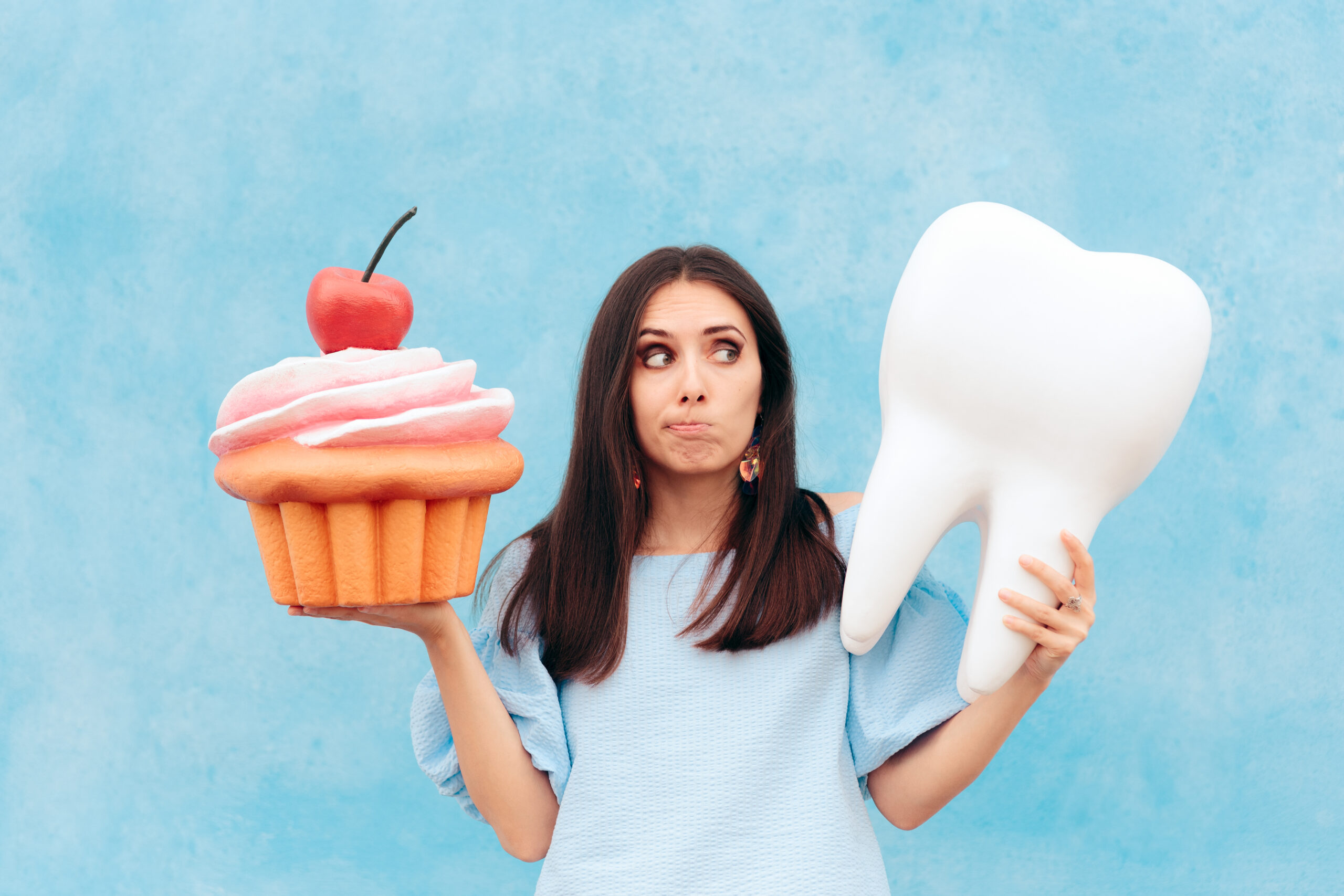 Woman holding a fake tooth and cupcake.