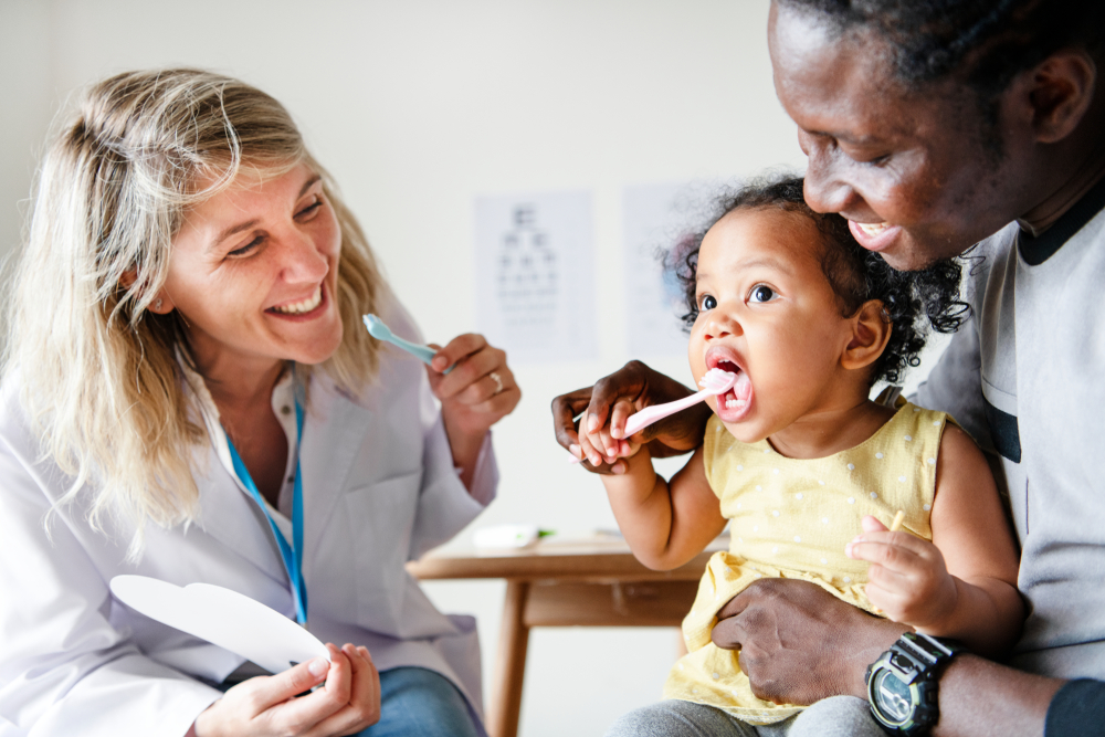 dentist showing toddler how to brush their teeth during their first dental visit